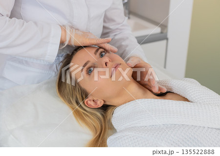 Young woman facial skin check by cosmetologist in gloves before planned relaxing cosmetic procedure 135522888