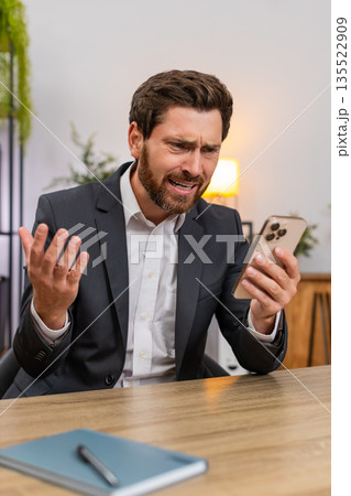 Middle-aged businessman frustrated reading client rejection on smartphone frowns at news loses game Middle-aged businessman frustrated reading client rejection on smartphone frowns at news loses game 135522909