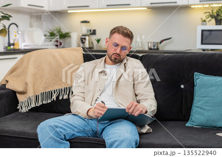 Young man drafts daily plan in notebook sets priorities makes schedule and maps tasks for week plans Young man drafts daily plan in notebook sets priorities makes schedule and maps tasks for week plans 135522940
