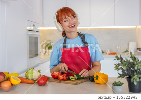 Young woman slices cucumber tomato on cutting board makes colorful salad and tastes fresh bite smile Young woman slices cucumber tomato on cutting board makes colorful salad and tastes fresh bite smile 135522945