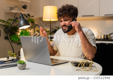 Arabian man with headset answers support call center client records ticket writes details at night 135522946