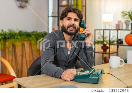 Indian man talks on retro wired telephone from nineties smiles places handset back on base with care 135522948