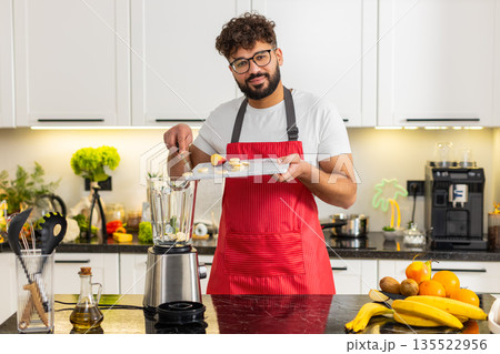 Arabian young adult man adding apple and banana to blender for smoothie breakfast in house kitchen Arabian young adult man adding apple and banana to blender for smoothie breakfast in house kitchen 135522956