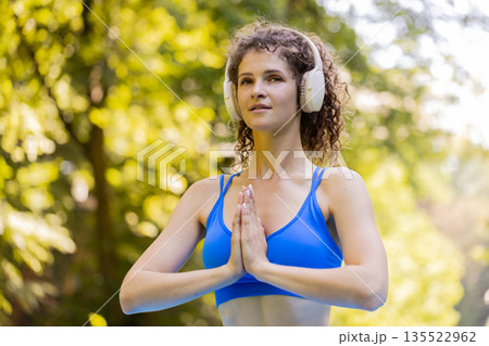 Woman sitting on mat in lotus position, relaxing practicing yoga meditation in park on summer day Woman sitting on mat in lotus position, relaxing practicing yoga meditation in park on summer day 135522962