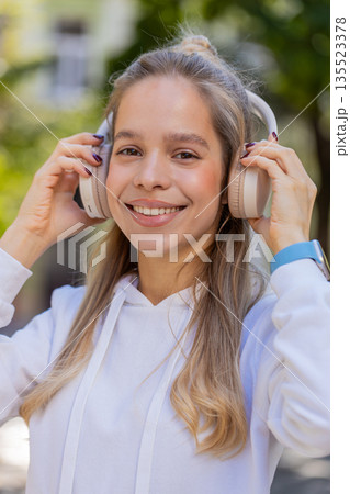 Happy young woman taking off headphones after listening favorite energetic music on city street Happy young woman taking off headphones after listening favorite energetic music on city street 135523378