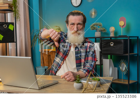 Senior man working on laptop computer at home office showing thumbs down sign dislike disapproval Senior man working on laptop computer at home office showing thumbs down sign dislike disapproval 135523386