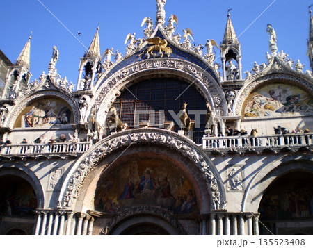 View of St. Mark s Basilica with its ornate domes and detailed fa ade set against a clear blue sky in Venice, Italy. Iconic example of Byzantine architecture and one of the most famous landmarks of View of St. Mark s Basilica with its ornate domes and detailed fa ade set against a clear blue sky in Venice, Italy. Iconic example of Byzantine architecture and one of the most famous landmarks of 135523408