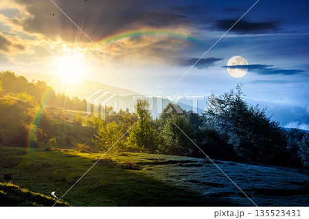 mountain landscape in fog. day and night time change concept. lush green alpine meadows in spring with sun and moon at twilight. beautiful view in to the valley. seasonal equality and shift template 135523431