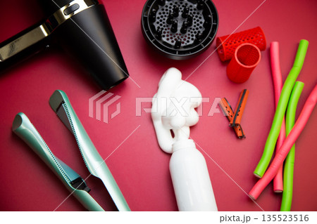 Top view on a pink background, a hairdryer with attachments, stylers and curling irons for straightening and creating curls, foam for creating volume and long-term holding, curlers of different shapes 135523516