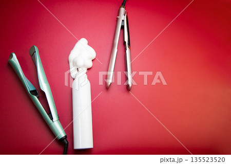 On the side there is a white bottle of styling foam, around it there is a straightener and a curling iron to create hair curls on a pink background with space for text. The concept of hair care 135523520