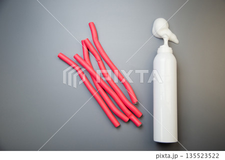 On the side, on a gray background, there is a bottle of foam for long-term hair styling, white foam poured out of it, pink bendable curlers with space for text lie nearby. The concept of styling 135523522