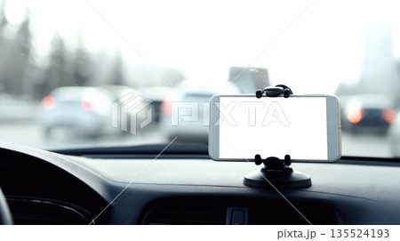 Blank smartphone screen mounted on car dashboard holder with blurred traffic background 135524193