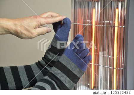 電気ストーブで暖をとる老人の足 135525482