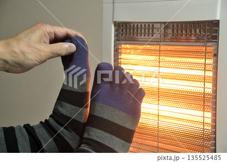 電気ストーブで暖をとる老人の足 135525485