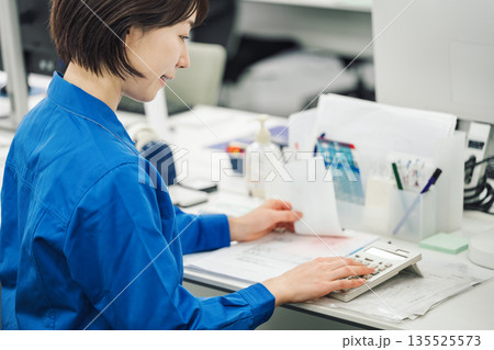 領収書を電卓で計算する作業服姿の若い女性 135525573
