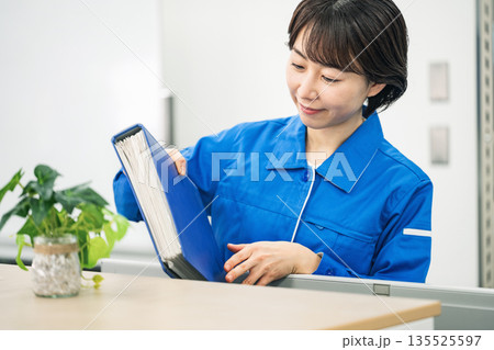 オフィスで書類を整理する作業服姿の若い女性 135525597
