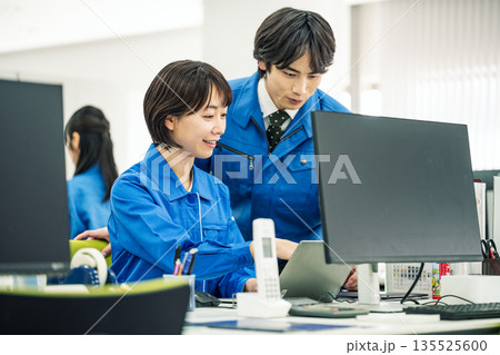 オフィスで同僚と話し合う作業服を着た若い女性 135525600
