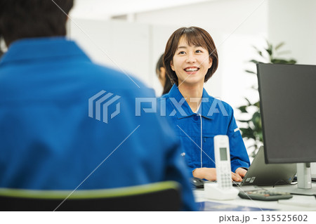 オフィスでデスクワークをする作業服を着た若い女性 オフィスでデスクワークをする作業服を着た若い女性 135525602