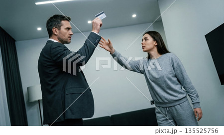 man and woman are in a modern living space discussing a financial document. The man holds a card while the woman reaches out showing signs of tension. man and woman are in a modern living space discussing a financial document. The man holds a card while the woman reaches out showing signs of tension. 135525756