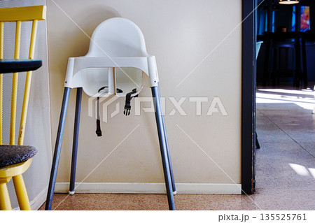Empty white baby high chair standing against a wall creating copy space. Empty white baby high chair standing against a wall creating copy space. 135525761
