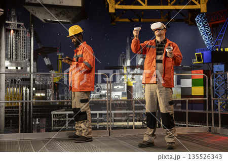 Male employee with VR glasses on offshore oil platform uses virtual reality tech to simulate drilling operations and monitor machinery, ensuring safety protocols in petroleum extraction. 135526343