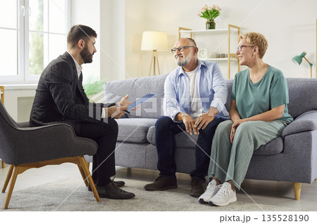 Mature couple consulting with professional advisor in comfortable living room 135528190