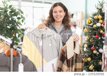 Young girl choosing coat or jacket in clothing store during Christmas Young girl choosing coat or jacket in clothing store during Christmas 135529392