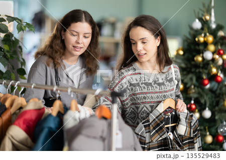 Two women choosing outerwear in a store against the background of a Christmas tree 135529483