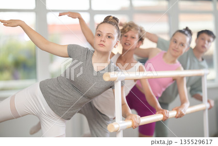 Teenagers ballet lovers learn to perform arabesque pose in choreography studio Teenagers ballet lovers learn to perform arabesque pose in choreography studio 135529617