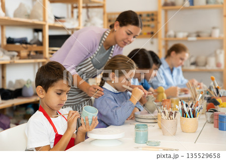 Attentive little boy painting handmade ceramic cup with brush Attentive little boy painting handmade ceramic cup with brush 135529658