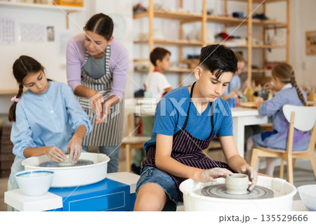 Boy in an apron working at a potter's wheel Boy in an apron working at a potter's wheel 135529666