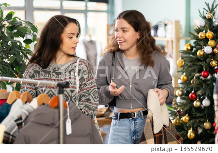 Two women choosing outerwear in a store against the background of a Christmas tree 135529670