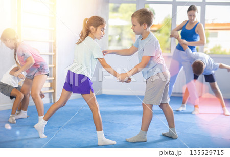 Children practicing in pair self-defence movements with female trainer supervision 135529715