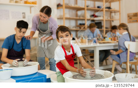 Boy in an apron working at a potter's wheel Boy in an apron working at a potter's wheel 135529744