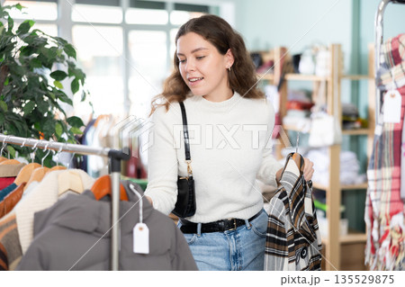 Woman holding a hanger with outerwear in her hands in a store 135529875