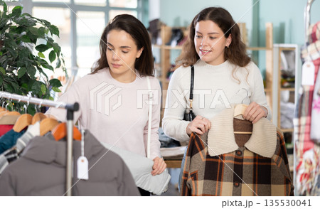 Female friends standing in the store and choosing outerwear Female friends standing in the store and choosing outerwear 135530041