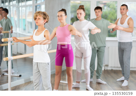 Teenage boys and girls practicing second position of ballet in dancehall 135530159