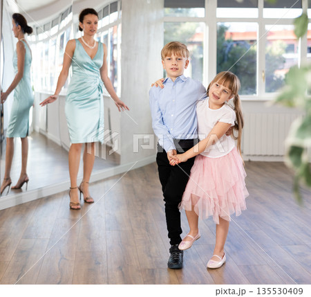Cheerful tween girl and boy rehearsing jive in dance studio with choreographer 135530409