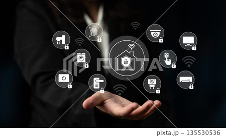 Woman in Business Suit Demonstrating Smart Home Technology with Various Connected Devices and Security Features in a Dark Background Gantry 135530536