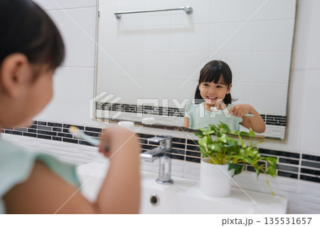 girl child brushing teeth at reflection in mirror in bathroom 135531657