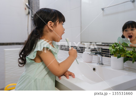girl child brushing teeth at reflection in mirror in bathroom 135531660