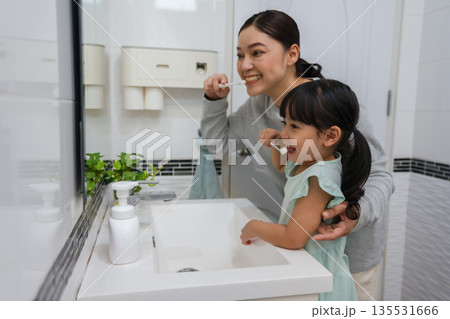 mother teaching girl child to brushing teeth and tongue at reflection in mirror in bathroom mother teaching girl child to brushing teeth and tongue at reflection in mirror in bathroom 135531666