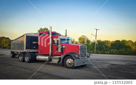 bold red semi truck with a long trailer sits in an open lot during sunset. The powerful rig highlights industrial design, chrome accents, and the rugged appeal of transportation and logistics bold red semi truck with a long trailer sits in an open lot during sunset. The powerful rig highlights industrial design, chrome accents, and the rugged appeal of transportation and logistics 135532005