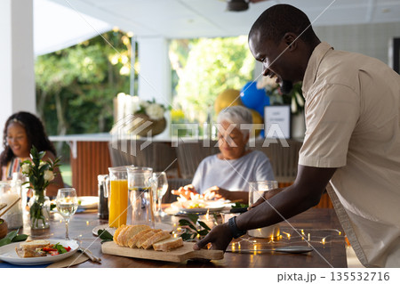 Serving fresh bread at family gathering, smiling and enjoying outdoor meal together 135532716
