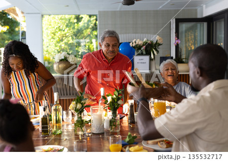 Family enjoying outdoor meal together, sharing laughter and conversation at table Family enjoying outdoor meal together, sharing laughter and conversation at table 135532717