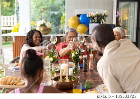 Family celebrating together outdoors, raising glasses in joyful toast at table 135532725