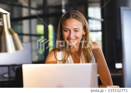 Smiling woman working on laptop at office, enjoying productive evening 135532771