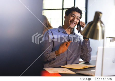 Smiling businessman on phone call, taking notes at modern office desk Smiling businessman on phone call, taking notes at modern office desk 135532780