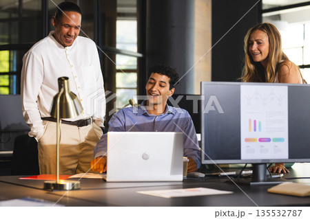 Team collaborating on laptop in modern office, discussing project with enthusiasm 135532787