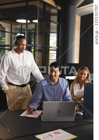 Collaborating in modern office, business professionals discussing project details on laptop Collaborating in modern office, business professionals discussing project details on laptop 135532797